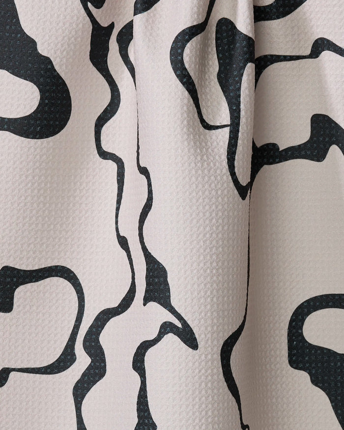 Close-up of the Marina Solodka "Monochrome Liquid" tea towel, showcasing its light color and abstract black wavy line design on ultra-absorbent textured fabric, with folds and shadows adding visual depth.