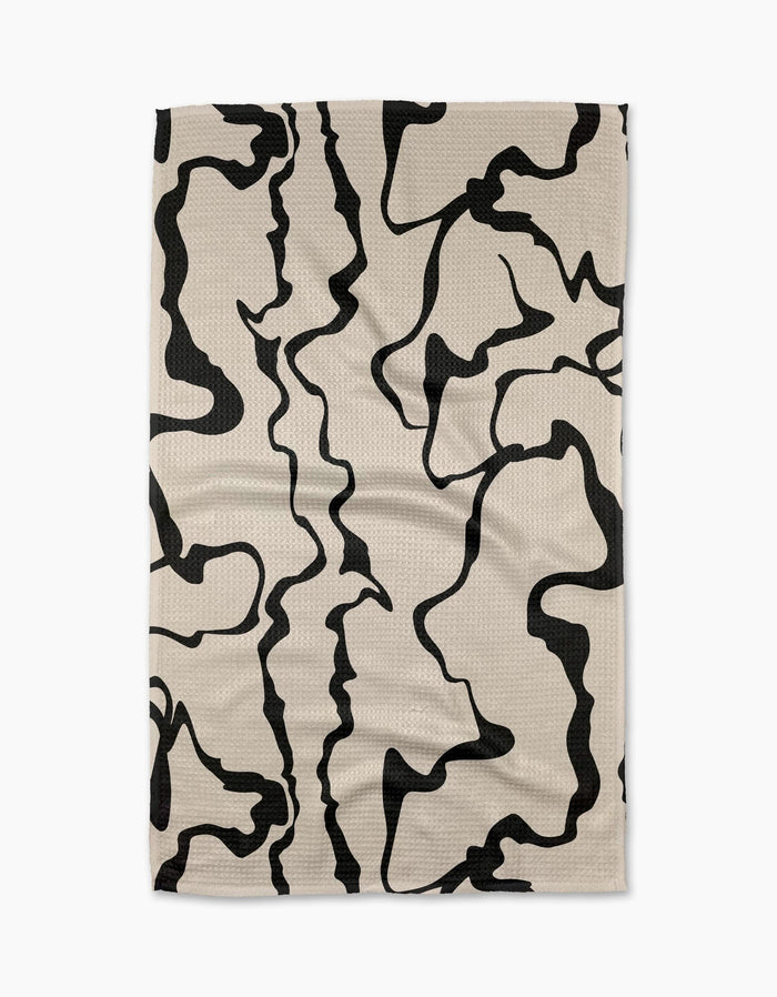 The Monochrome Liquid tea towel by Marina Solodka is beige, rectangular, made from recycled materials, and features an abstract black squiggly line pattern—shown laid flat on a white background.