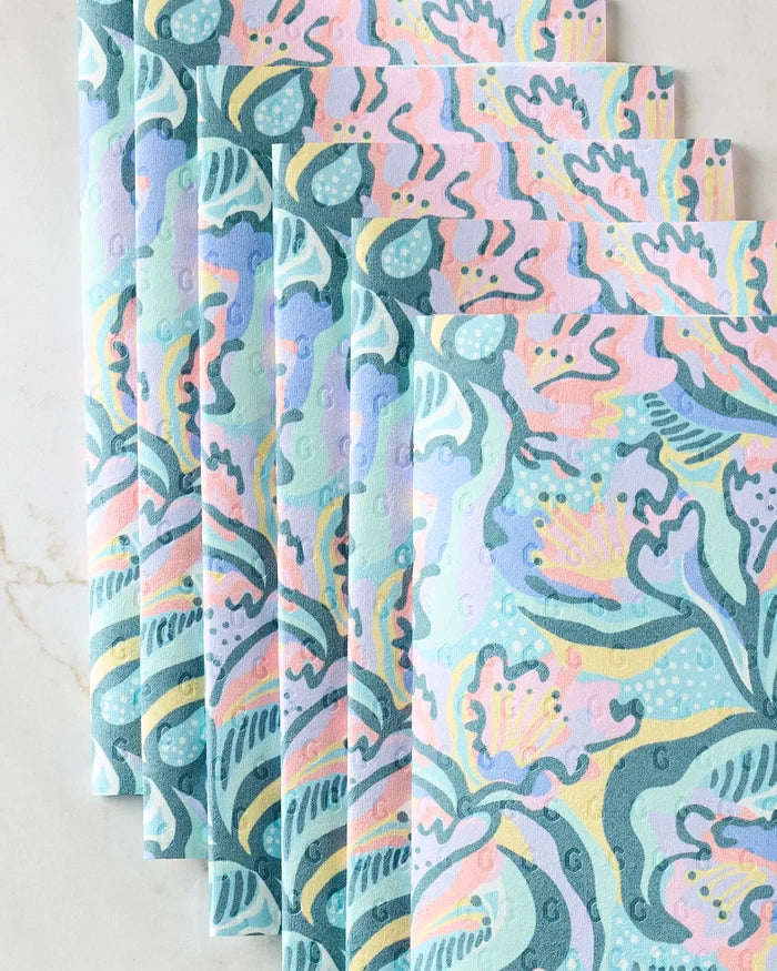 Six Moody Flowers eco-friendly paper towels by Masha Volnova, in pastel blue, pink, green, and yellow with floral and abstract patterns, are folded and arranged diagonally on a light marble surface.