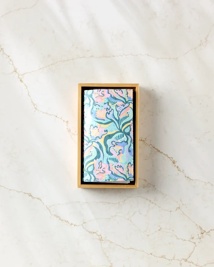 The Moody Flowers rectangular box by Masha Volnova, featuring a pastel floral-patterned lid, holds eco-friendly paper towels and is placed on a white marble surface with subtle brown veins.