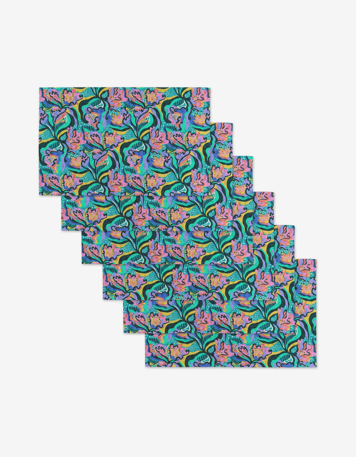 Six Moody Flowers rectangular placemats by Masha Volnova are stacked, each with a vibrant floral and leaf pattern in aqua, pink, purple, yellow, and green on a dark background—crafted from eco-friendly materials for sustainable style.