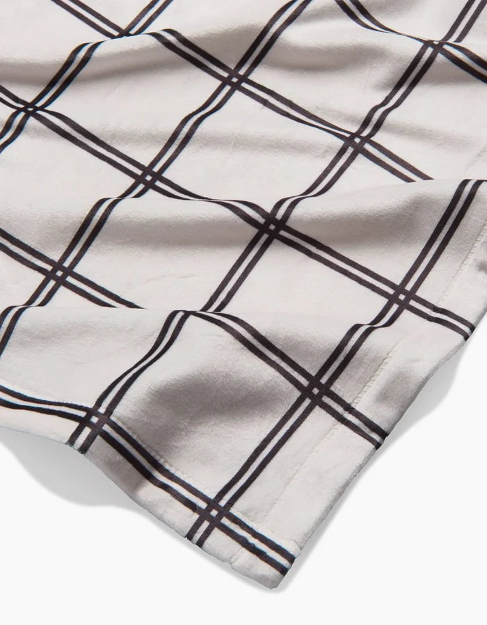 A close-up of Geometry’s Moon fabric, a soft white material with a black and brown windowpane plaid pattern, made from recycled materials and gently wrinkled on a flat surface.