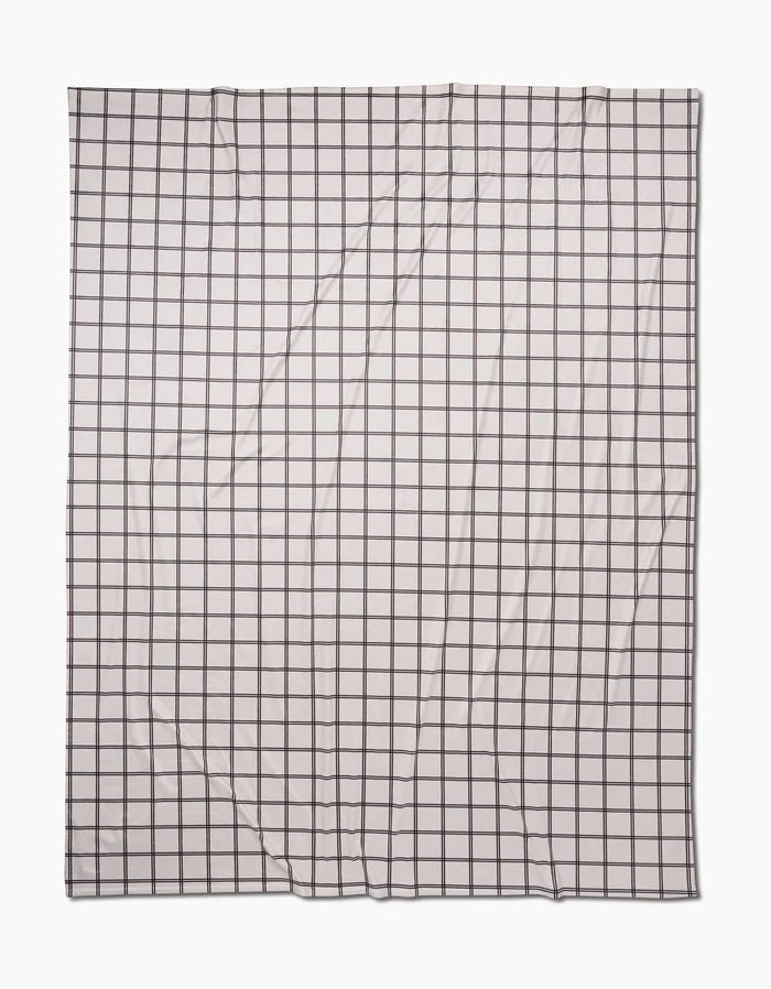 A rectangular, white Moon Butter Blanket by Geometry, made from recycled materials and featuring a black grid of evenly spaced lines, is laid flat with slight visible wrinkles.