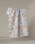 The Morning Blooms tea towel by Charlie Rowan Designs features orange and yellow florals on white, crafted from recycled materials and displayed against a neutral backdrop.