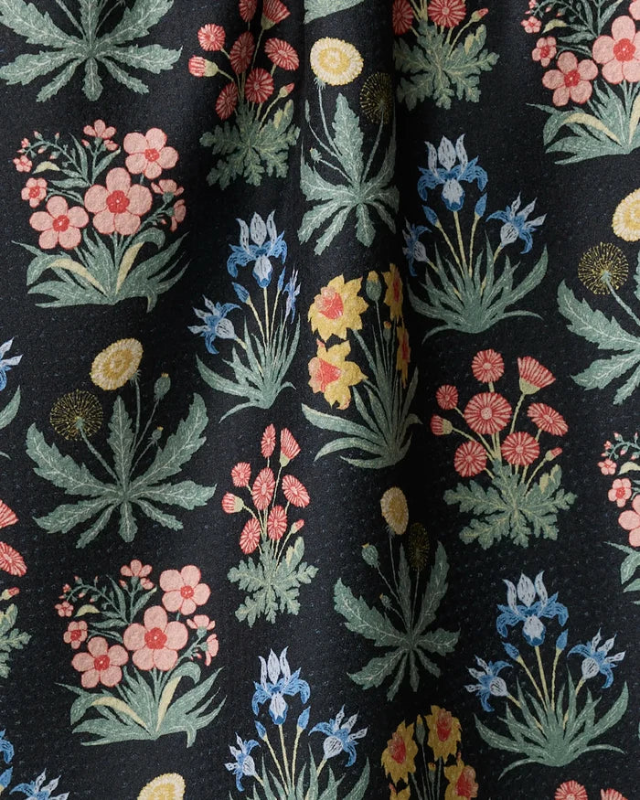 Morning Meadow by Danelys Sidron features a colorful floral pattern with clusters of pink, blue, yellow, and red flowers with green leaves on a black background. Made from recycled materials, this fabric drapes in gentle folds.