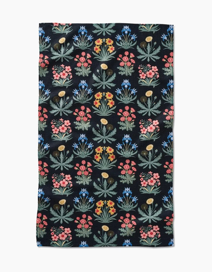 The Morning Meadow Tea Towel by Danelys Sidron features a black rectangular design with rows of vibrant, stylized red, yellow, blue, and green flowers on durable Geoweave™ fabric.