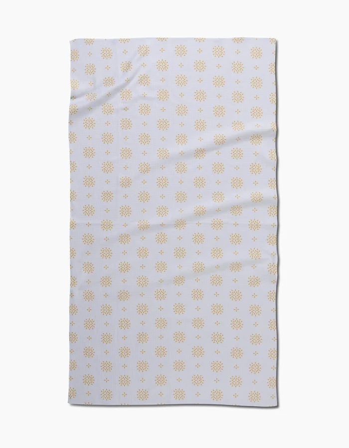 The Danelys Sidron Morning Petals bath towel is rectangular and white, featuring a repeating pattern of small yellow sunbursts. Slightly wrinkled, the towel is displayed on a plain white background.