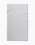 The Danelys Sidron Morning Petals bath towel is rectangular and white, featuring a repeating pattern of small yellow sunbursts. Slightly wrinkled, the towel is displayed on a plain white background.