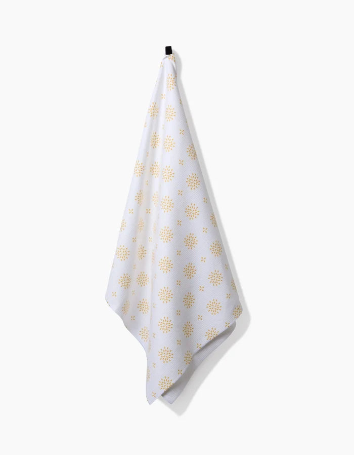 The Morning Petals Luxe Bath Towel by Danelys Sidron, featuring yellow sunburst shapes and crafted with Geoweave technology for superior absorbency and quick drying, hangs from a black hook against a plain white background.