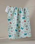 The "Mother" tea towel by Sarah Holden is a blue, quick-drying towel made from recycled materials. It features playful butterflies, lips, stars, dice, hearts, and the word MOTHER—perfect for daily indoor use.