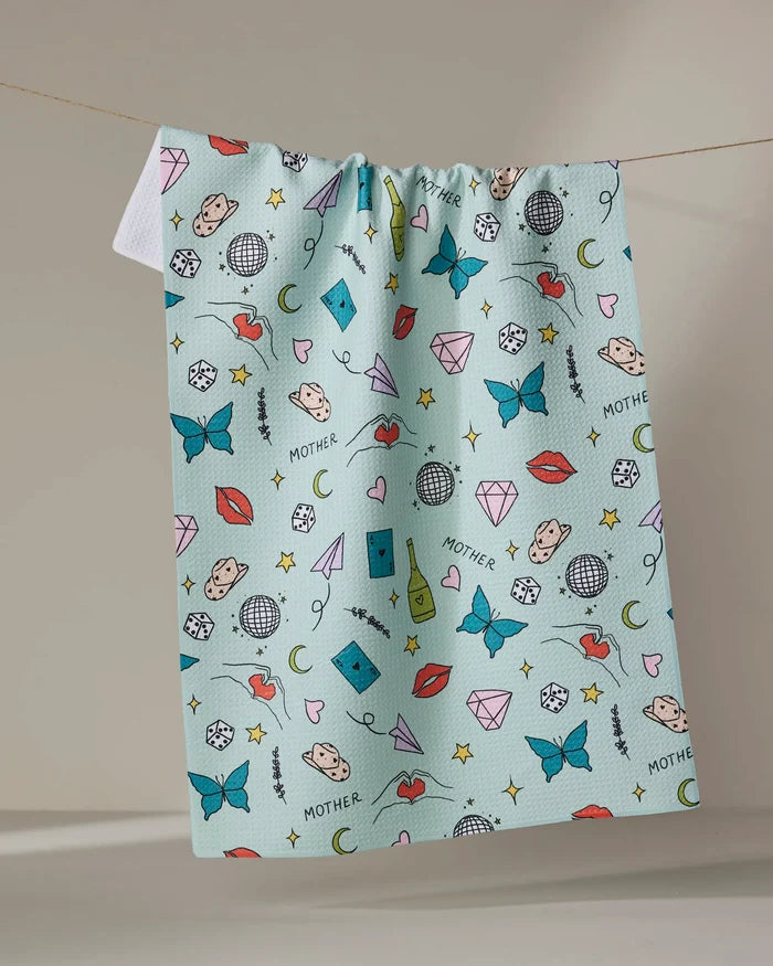 The "Mother" tea towel by Sarah Holden is a blue, quick-drying towel made from recycled materials. It features playful butterflies, lips, stars, dice, hearts, and the word MOTHER—perfect for daily indoor use.