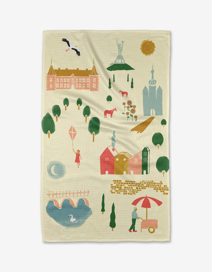 The Motherland Tea Towel by Elisabeth Wing, illustrated with vibrant houses, trees, and a castle, is crafted from sustainable Geoweave fabric in light beige—adding a charming, eco-friendly touch to your kitchen.