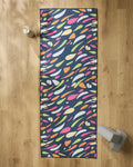 The GEOMETRY Motion yoga mat features a colorful abstract pattern on a dark background. Shown on a wooden floor with a non-slip yoga towel, water bottle, and gray yoga block.