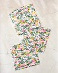 Three folded Moxie Mauve recycled dishcloths by Lisa Nelson, featuring a bright floral pattern with green leaves and pink and yellow flowers, are arranged on a light beige marble surface.