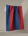 The Modern Dad’s Mr. Rugby tea towel, featuring quick-drying fabric and vertical blue and maroon stripes, hangs on a clothesline against a plain light background.