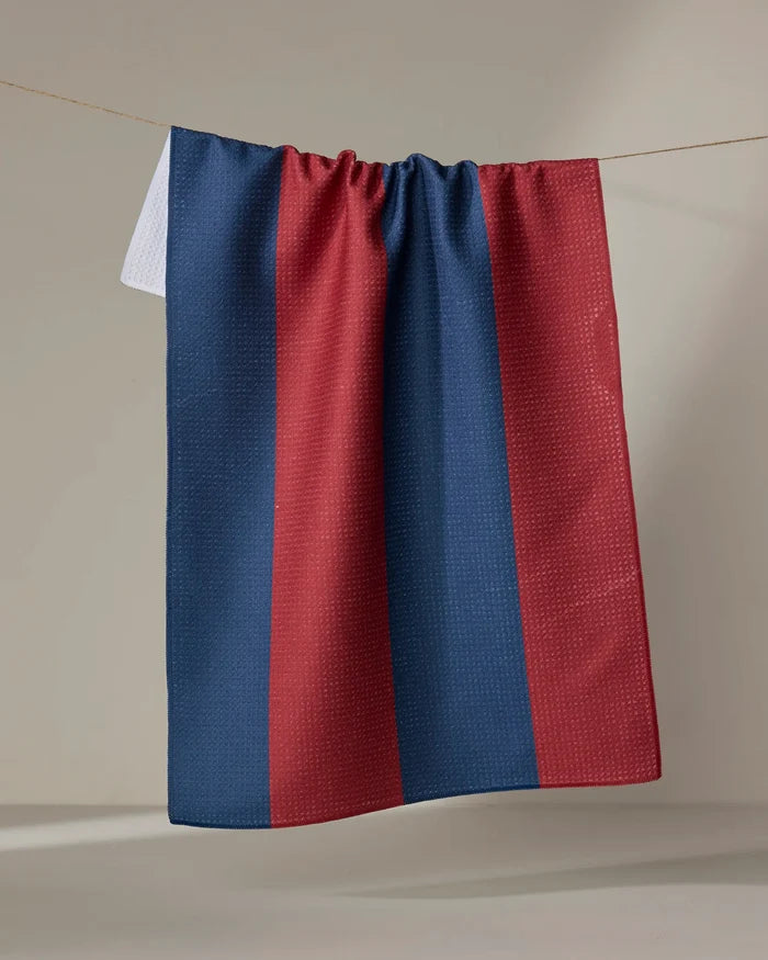 The Modern Dad’s Mr. Rugby tea towel, featuring quick-drying fabric and vertical blue and maroon stripes, hangs on a clothesline against a plain light background.