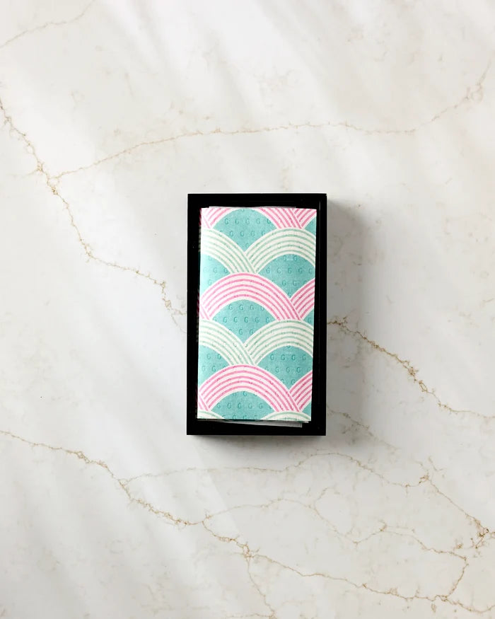 The Nalin bar by Amy MacCready, wrapped in pastel blue and pink patterned recycled paper towels, rests in a black tray on a light marble surface.