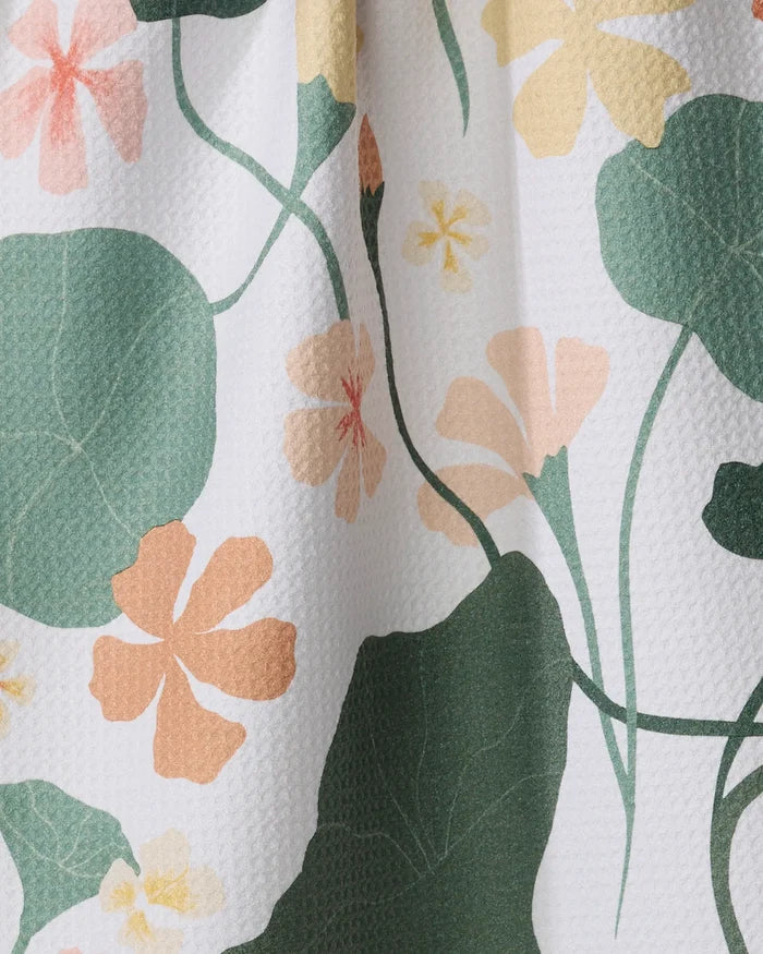 Close-up of Elana Gabrielle's Nasturtiums recycled kitchen towel, showing a textured white background with green leaves and pastel orange, yellow, and pink floral patterns.