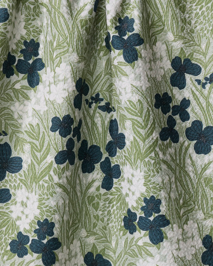 Katie O'Shea's "Navy And Sage Meadow" features a green and white leafy background with dark blue floral designs. Folds in this recycled kitchen towel add subtle shadows and textured detail.