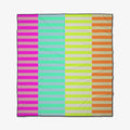 The GEOMETRY Neon Nights Beach Blanket showcases horizontal stripes in bright pink, turquoise, yellow, and orange divided by a center line. Its sand-repelling and quick-drying features make it ideal for beach days.
