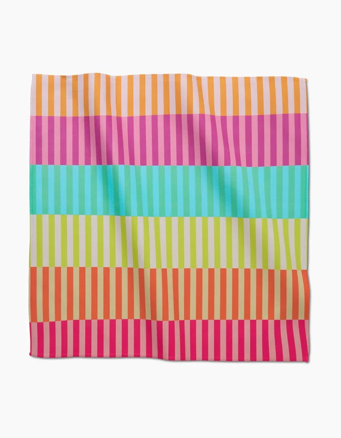 The GEOMETRY Neon Nights Dinner Napkin is a square Geosuede cloth with bold horizontal stripes in orange, pink, turquoise, green, and red, overlaid by lighter vertical lines. Made from recycled materials.