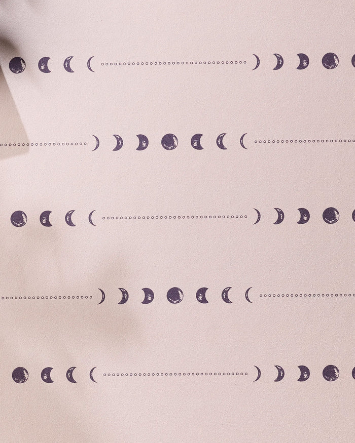 The Night Sky yoga towel by Ashley Celena features a calming beige background with rows of small purple moon phases—new, crescent, half, gibbous, and full—separated by dotted lines for a non-slip experience.