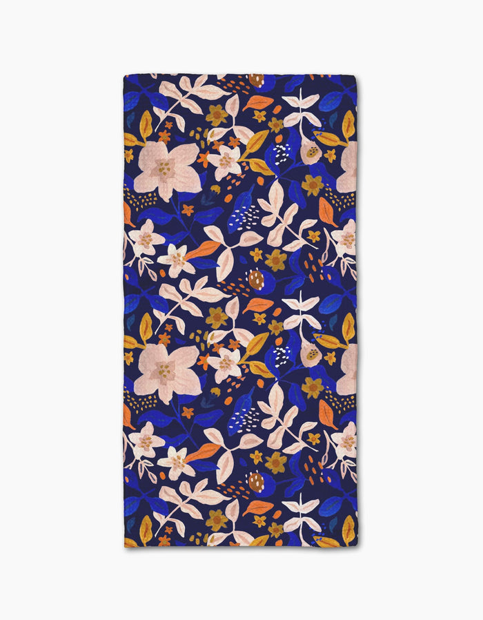 The Nightfall Garden towel by Cottonflower Studio is rectangular, ultra-absorbent, and features a bold floral pattern with pink, white, and orange flowers and leaves on a dark blue background.
