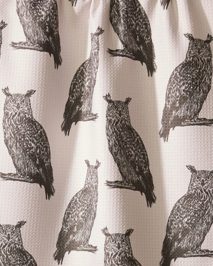 The Geometry Nocturne recycled kitchen towel showcases repeated black owl prints on a light, textured background. A center owl is uniquely distorted by a fabric fold.