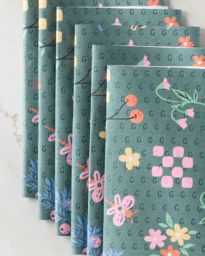 North Meadow Bright Night napkins by Charlie Rowan Designs feature green fabric with pink, orange, and yellow floral patterns. Fan-shaped on a light surface, these reusable napkins are an eco-friendly alternative to paper towels.