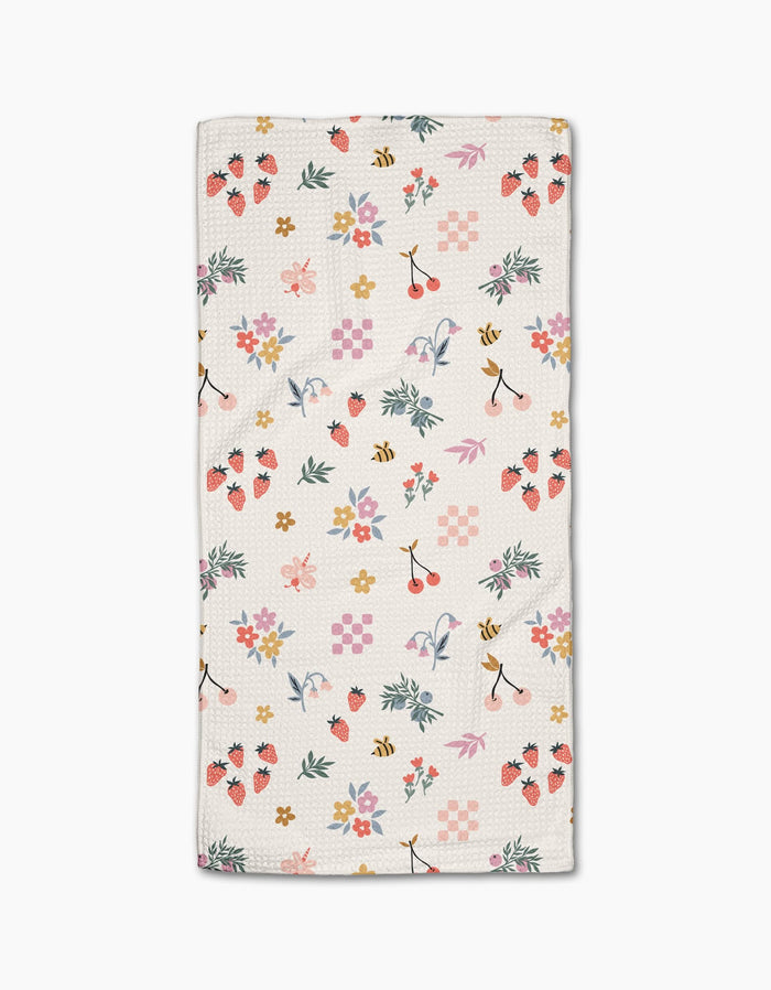 The North Meadow Morning Bar Towel by Charlie Rowan Designs features a colorful pattern of strawberries, cherries, bees, flowers, leaves, and shapes in pink, yellow, green, and purple on white—crafted from sustainable recycled materials.
