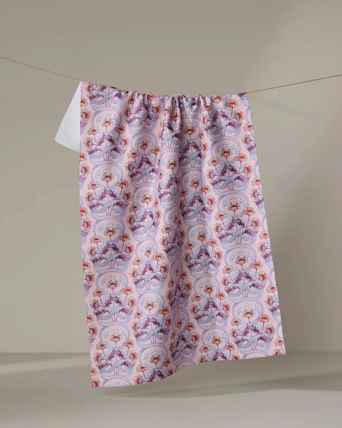 The Nouveau Snake kitchen towel by Maayan Alper-Swan, featuring eco-friendly fabric and vibrant pink, purple, and red floral and geometric patterns, hangs on a line against a neutral beige background.