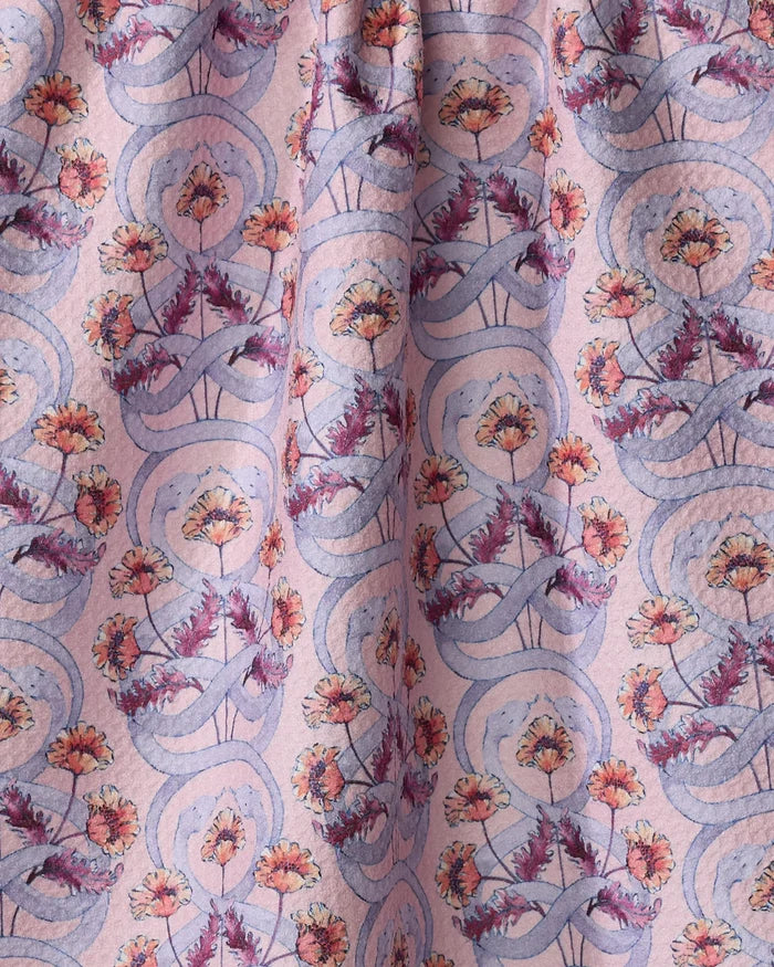 Close-up of eco-friendly pink Nouveau Snake fabric by Maayan Alper-Swan, featuring orange and yellow flowers with blue swirling lines. Softly draped, it’s ideal for a decorative kitchen towel or tea towel.