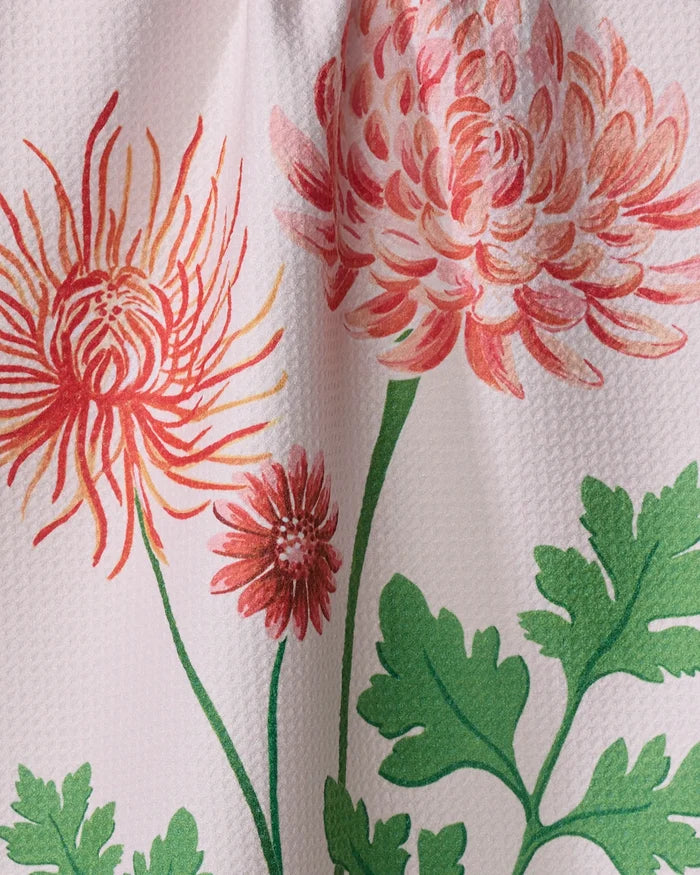 Close-up of the Linda Fox "November Chrysanthemum" dish towel, featuring large pink and orange chrysanthemum flowers and green leaves on a textured white background.