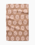 The “Nuts About You” tea towel by Aubrey Fairchild features a brown and beige circular squirrel design over small diamonds. Made of quick-drying fabric, it appears slightly wrinkled and is displayed on a white surface.
