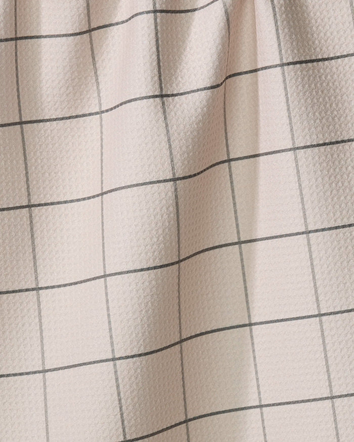 The Oat Grid tea towel by Kelsi Fullmer features a light pink hue and black grid pattern. Made from recycled materials, it has gentle folds and a softly textured, dimpled surface.
