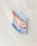 Nine "Oceans" folded napkins by Ceyda Alasar, featuring vibrant seaweed, coral, and fish designs, are arranged on marble—a stylish, eco-friendly alternative to paper towels for your table.