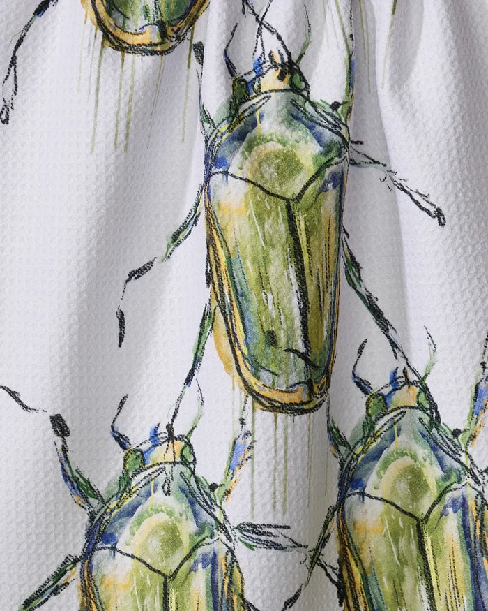 A close-up of the Olive Beetles tea towel by Taryn Brennan, showcasing a white textured fabric with green and yellow beetle illustrations outlined in dark lines in a scattered, overlapping pattern.