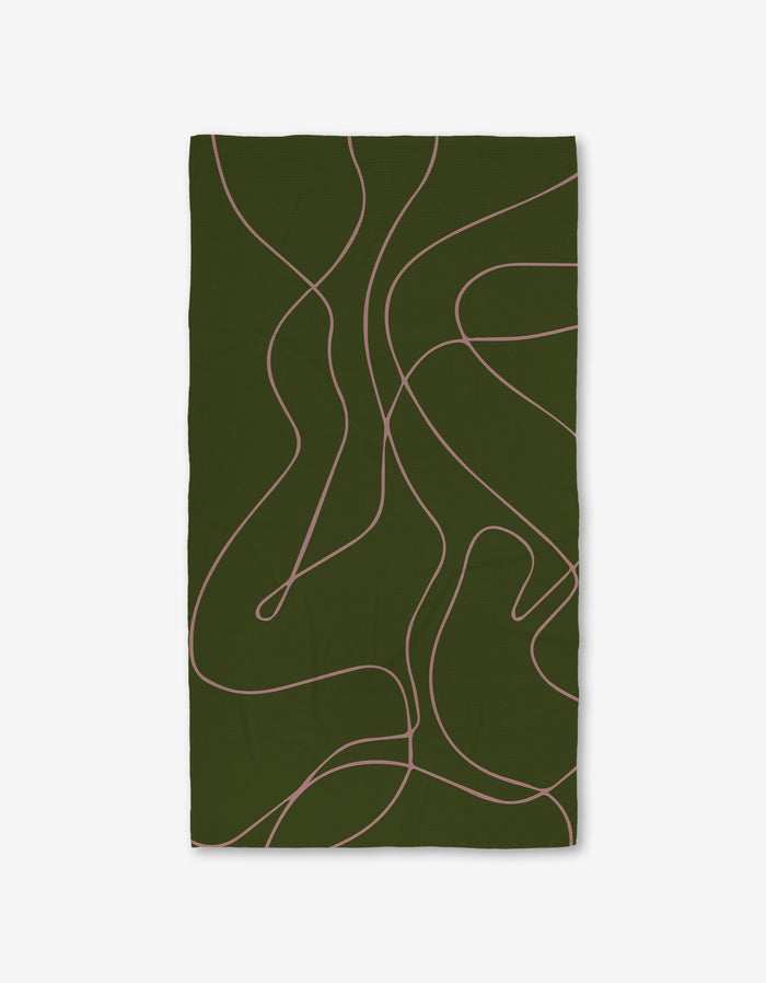 The GEOMETRY Olive Martini is a rectangular dark green blanket with thin, wavy light pink lines. Its made from ultra-absorbent post-consumer recycled materials and shown against a plain white background.