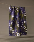 The Oliveberry skirt by Geometry, knee-length with a gathered waistband, made from quick-drying recycled materials and adorned with a blue and olive green abstract floral print, hangs from a clothesline against a neutral background.
