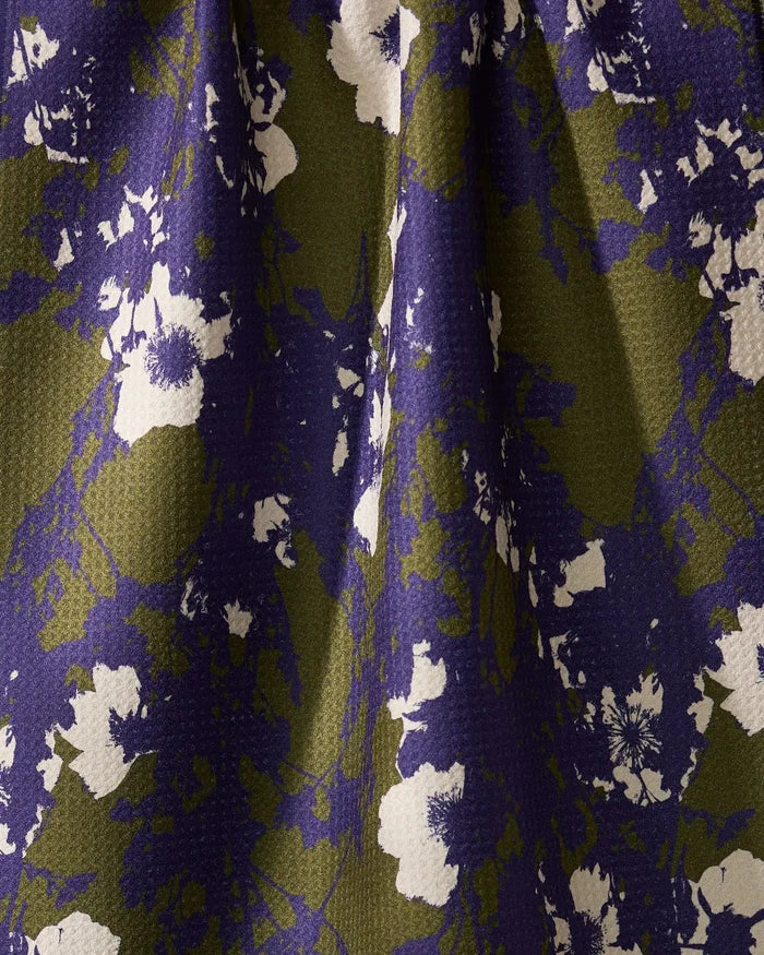 A close-up of Geometrys Oliveberry tea towel, crafted from quick-drying recycled materials. It features a softly pleated, textured surface with an abstract floral pattern in white, purple, and olive green.