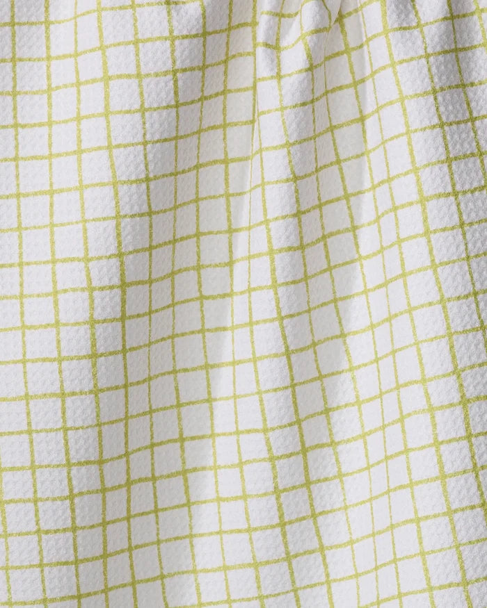 The On the Lawn kitchen towel by Kayla Ann is white with a textured finish and a grid pattern of thin light green lines, creating soft folds and subtle shadows.
