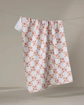 The Orange Checker tea towel by Teri the Butter, featuring a quick-drying checkered pattern with orange floral designs, hangs on a clothesline against a simple background.