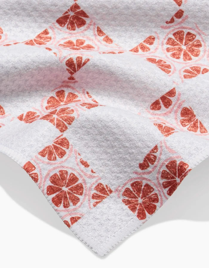 The Orange Checker by Teri the Butter is a white Geoweave bar towel made from recycled materials, featuring a grid of solid white squares and orange slice prints. The fabric’s folds and shadows add depth to the checkerboard pattern.