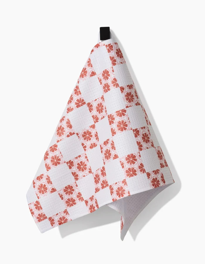 A kitchen towel by Teri the Butter, called Orange Checker, made from Geoweave fabric with an orange checker pattern and a black hanging loop, draped against a white background.
