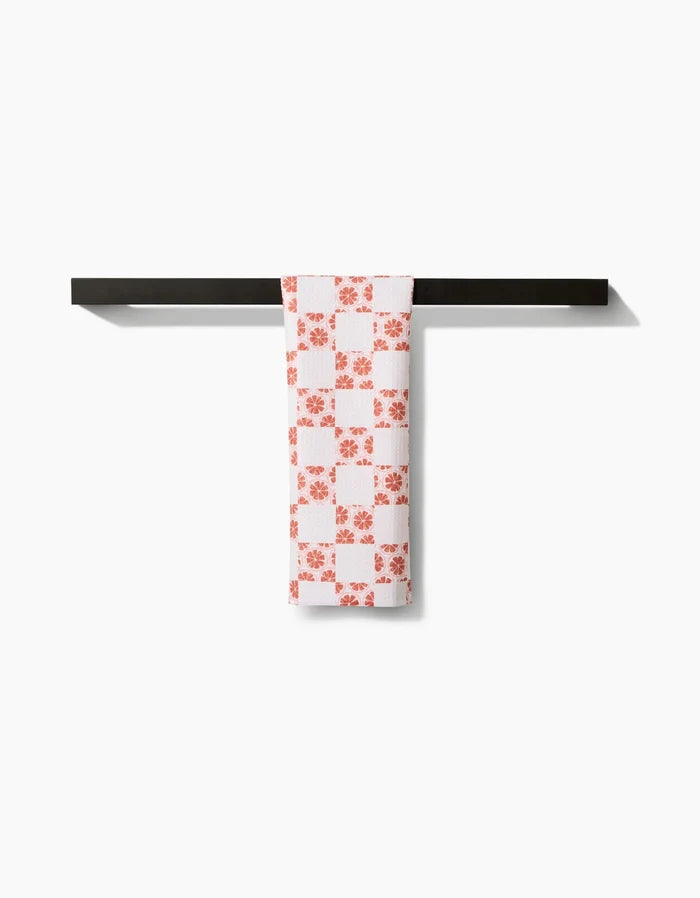 The Orange Checker by Teri the Butter, an orange checkered bar towel made from recycled materials, hangs neatly over a black towel bar against a plain white background.