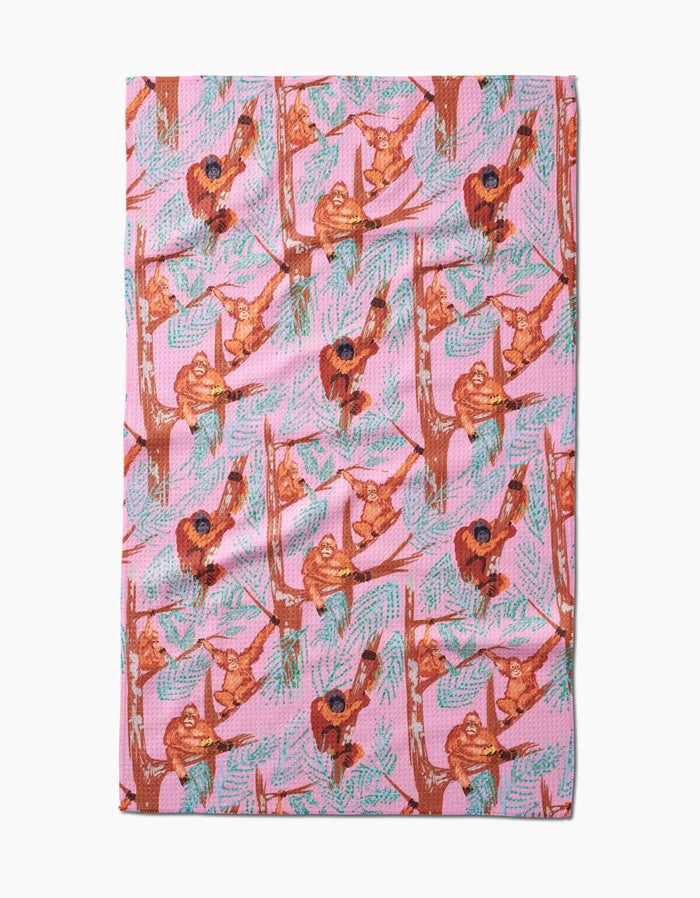 The Orangutan Clan tea towel by Elisabeth Wing features illustrated orangutans on tree branches with green leaves, printed on soft Geoweave fabric made from recycled materials.
