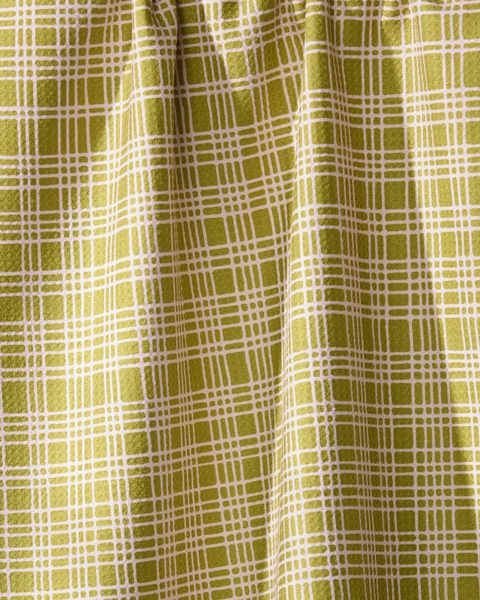 A detailed view of Geometry’s Orchard Plaid Green curtain features a yellow-green grid reminiscent of a tea towel. The eco-friendly fabric is gathered at the top, forming soft vertical folds.