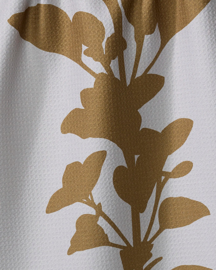 A close-up of PrintedPlant’s Oregano tea towel, crafted from recycled materials, shows its bold golden-brown botanical silhouette pattern with striking leaves and stems on textured white fabric.