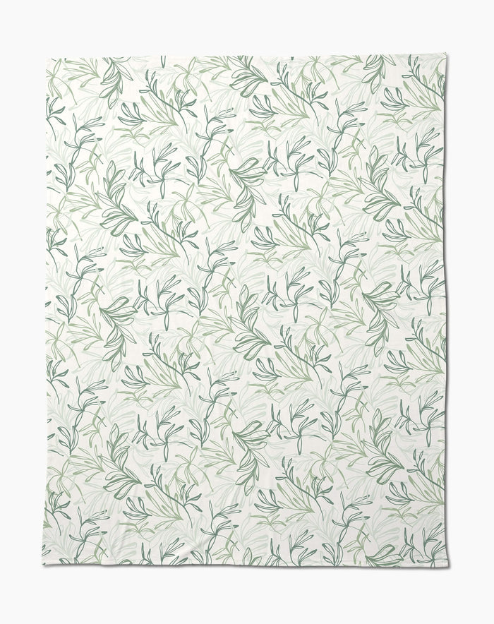 The Organic Foliage Butter Blanket by Kris Ruff is white, silky soft, and features a subtle repeating pattern of green leafy branches and vines for a delicate botanical look.