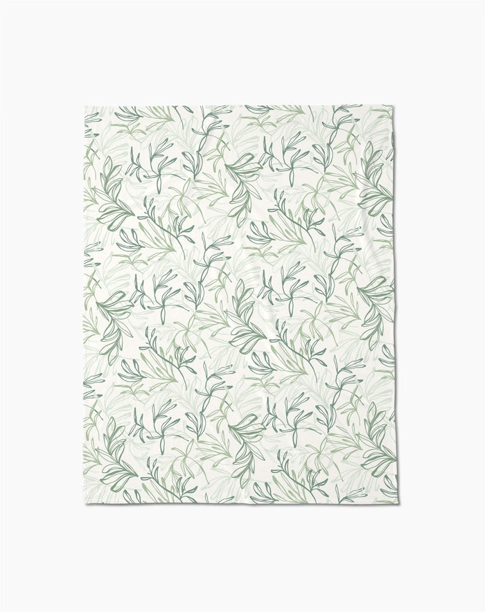 The Organic Foliage Butter Blanket by Kris Ruff features a delicate green and gray leafy branch pattern on white, crafted from recycled materials for silky softness.